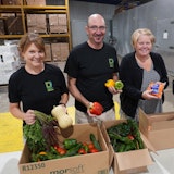 Three volunteers smiling while packing boxes of food.